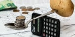 Coins balanced on a spoon, weighted by a potato on a calculator