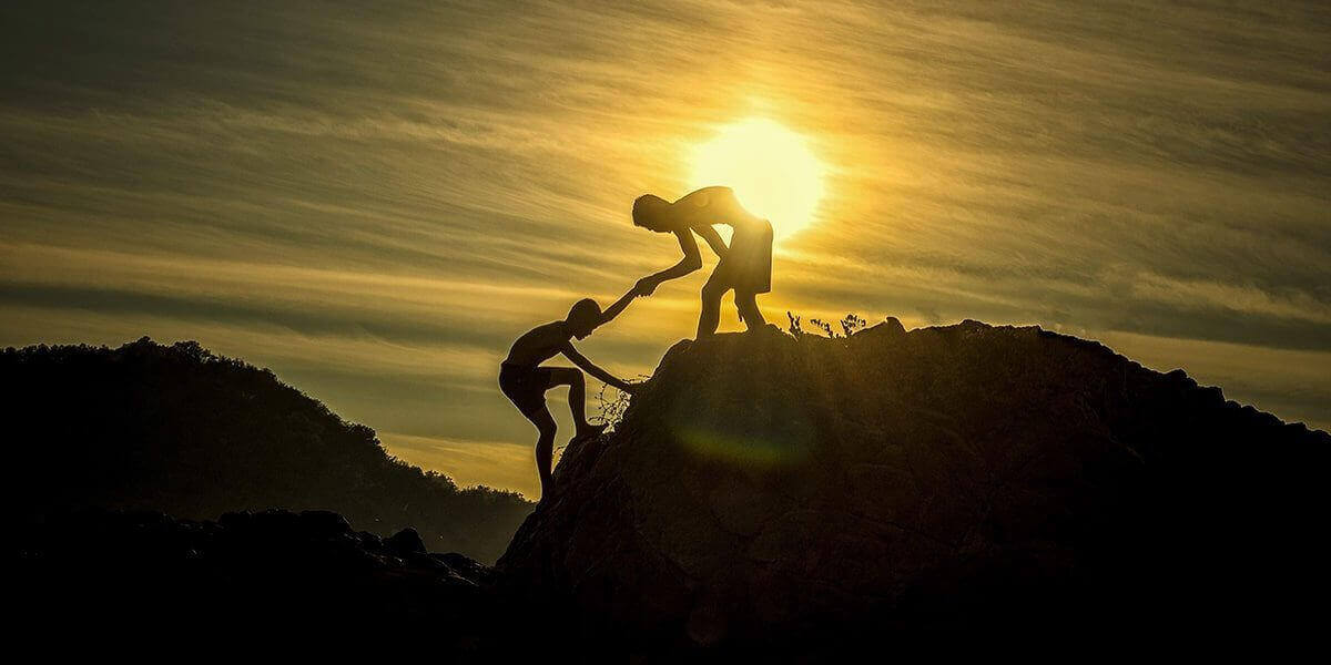 Two boys helping each other climb a mountain