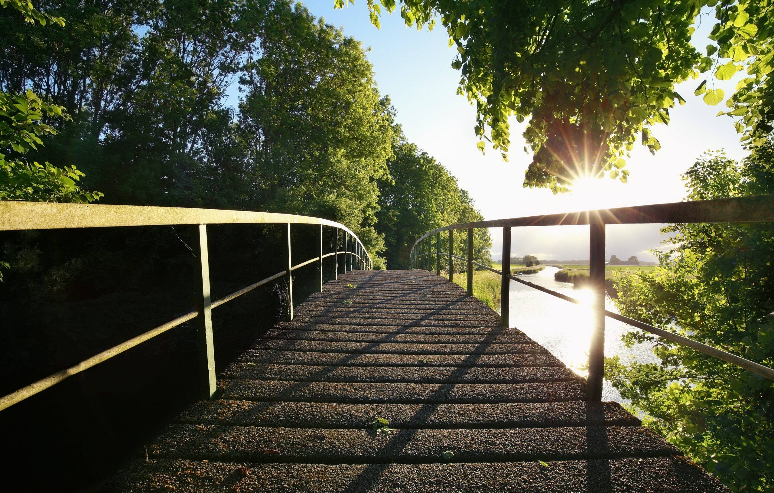 wooden bridge via river on sunny day